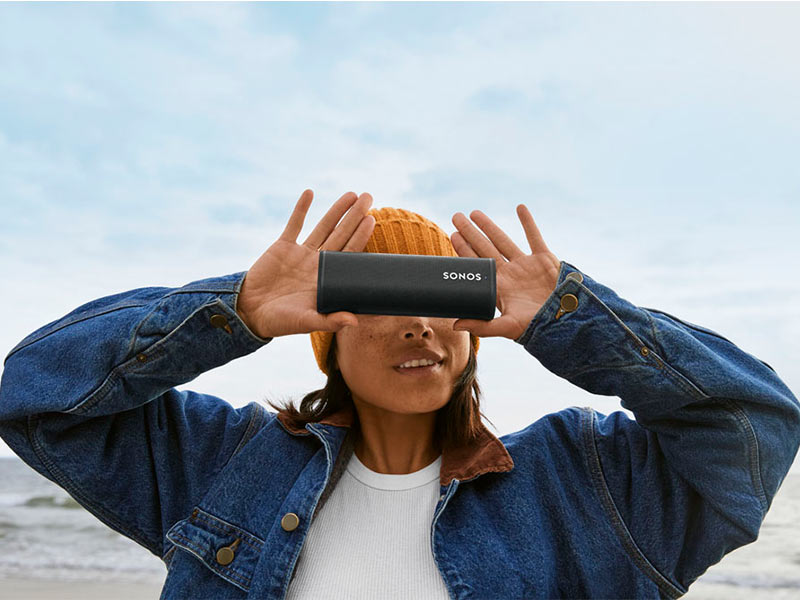 Sonos Roam Bluetooth-Lautsprecher in schwarz gehalten vor Gesicht einer Person.