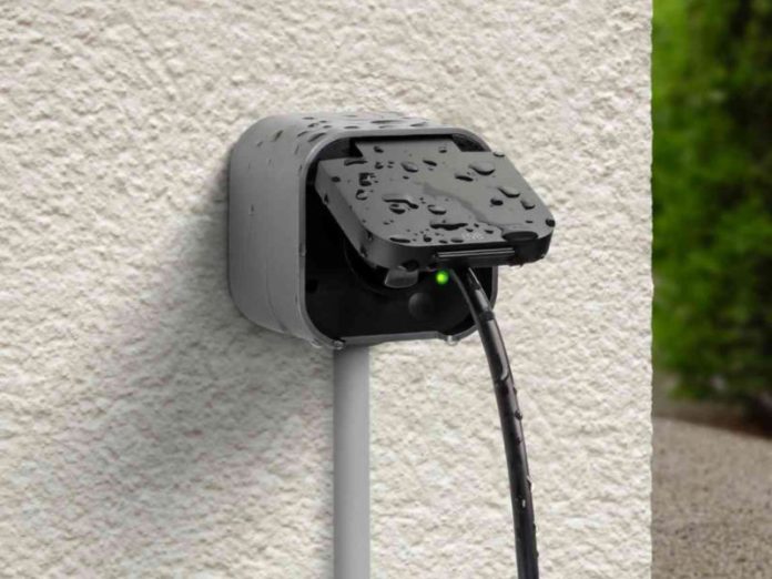 Eve Energy Outdoor an der Hauswand mit eingestecktem Stecker, Regentropfen auf der Abdeckung. Dies ist eine der besten Outdoor-Steckdosen.