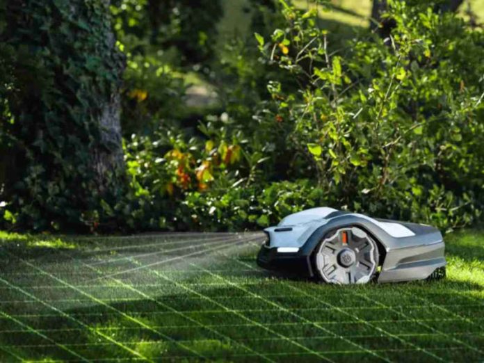 Husqvarna Automower 405VE Nera fährt den Rasen ab, KI-Sicht wird visuell dargestellt mit Gittermuster auf dem Rasen. Im Hintergrund Sträucher und ein Baum.