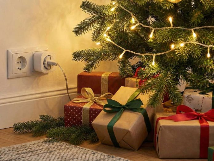 Lichterkette vom Weihnachtsbaum ist in eine smarte Steckdose gesteckt, um den Baum herum liegen eingepackte Geschenke