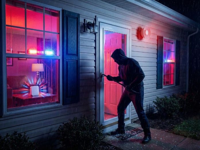 Ein Einbrecher versucht in einer regnerischen Nacht in ein Haus einzudringen, während der SmartThings Home Monitor Alarmleuchten (hellrot und blau) und die Außensirene auslöst.
