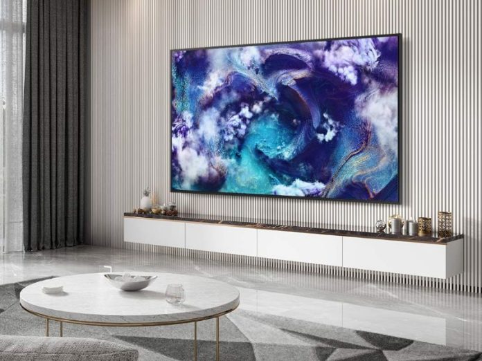 Großer Samsung-Fernseher SmartThings Hub an einer weißen Lattenwand, mit lebhaften blau-violetten und goldenen abstrakten Kunstwerken. Der Fernseher hängt über einem weißen schwebenden Sideboard in einem modernen, hellen Wohnzimmer.