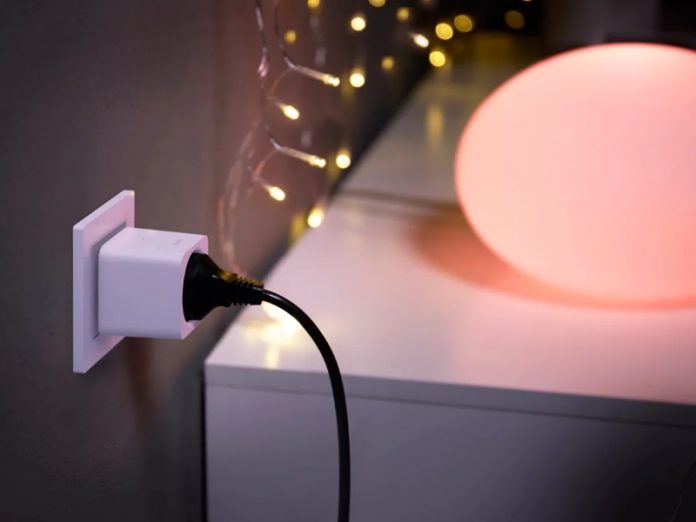 Weißer Smart Plug Adapter steckt in einer Steckdose, um die Apple Home Energiekosten zu überwachen. Im Hintergrund leuchtet eine große, rosa Kugel.