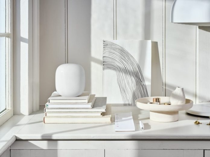 Weißer, abgerundeter WLAN Mesh Router auf einem Stapel Bücher in einem hellen, minimalistischen Interieur.