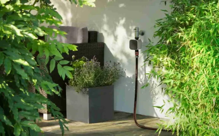Eve Aqua am Wasserhahn auf der Terrasse mit angeschlossenem Wasserschlauch zur smarten Gartenbewässerung