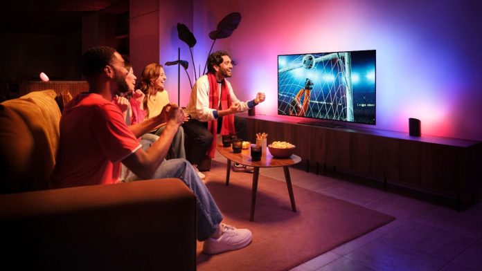 Freunde schauen gespannt ein Fußballspiel, während das Philips Hue WM Update den Raum in stimmungsvolles blaues und magentafarbenes Licht taucht.