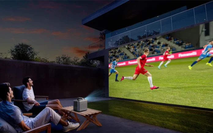 Zwei Männer sitzen draußen auf der Terrasse mit Tisch und Outdoor-Sesseln und schauen Fußball auf einer großen Projektionsfläche, mit Nebula X1 SE Beamer. So sieht Public Viewing zur WM im Garten aus.