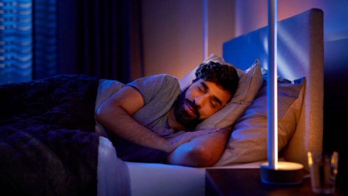 Ein Mann, der ruhig in einem dunklen Raum schläft, der vom sanften und warmen Schein der „Jetlag“-Smart-Beleuchtung erhellt wird, um den Schlaf-Wach-Rhythmus zu fördern.