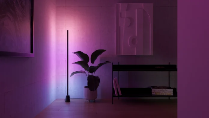 Ein modernes Zimmer mit einer schlanken Stehlampe, die einen stimmungsvollen violetten Schimmer auf die Wand im Beton-Look und eine Zimmerpflanze wirft.