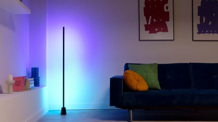 Eine schlanke Wiz-Stehlampe beleuchtet ein modernes Wohnzimmer mit einem stimmungsvollen violetten und blauen Schein neben einem dunkelblauen Sofa.
