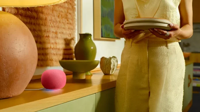 Ein rosa Google Home-Lautsprecher mit Gemini AI steht auf einer Kommode aus Holz in einem gemütlichen Interieur, während eine Person Teller in der Hand hält.