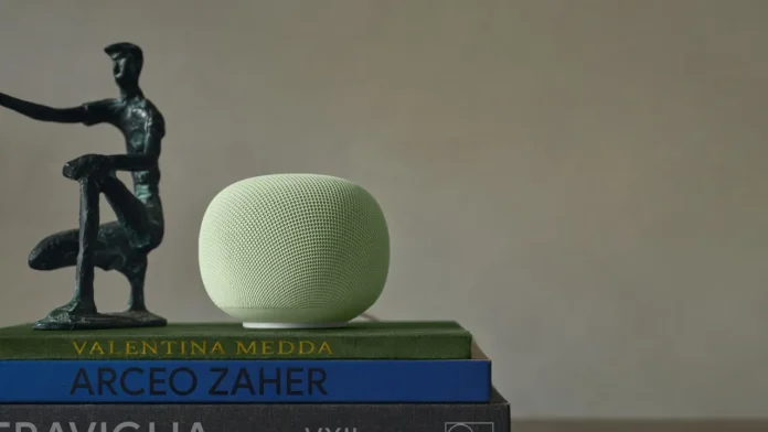 Ein hellgrüner Google Home-Lautsprecher mit Gemini AI steht auf einem Bücherstapel neben einer abstrakten Bronzeskulptur vor einem neutralen Hintergrund.