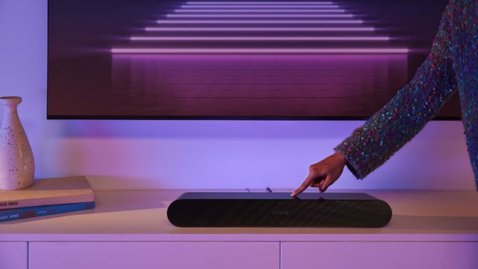 Ein Finger drückt auf die Taste einer schwarzen Sonos-Soundbar unter einem Fernseher mit violetter Neonbeleuchtung, um die Sonos-Soundbar mit einem neuen Router zu verbinden.
