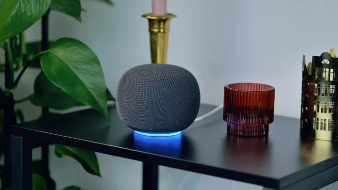 Google Home Speaker auf schwarzem Beistelltisch mit Teelichthaltern und Pflanze im Hintergrund, Lichtring vom Speaker leuchtet.