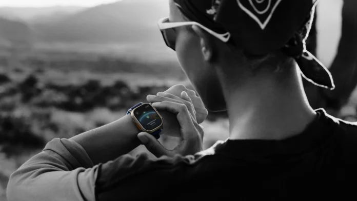 Ein Wanderer in einer rauen Berglandschaft betrachtet die Satellitenfunktionen auf einer robusten Apple Watch Ultra am Handgelenk.