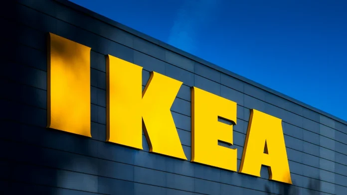 Großes gelbes IKEA-Logo an einer blauen Gebäudefassade vor strahlend blauem Himmel.