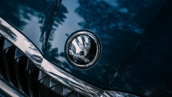 Nahaufnahme des silbernen Škoda-Logos auf der Motorhaube eines dunkelblauen Autos.