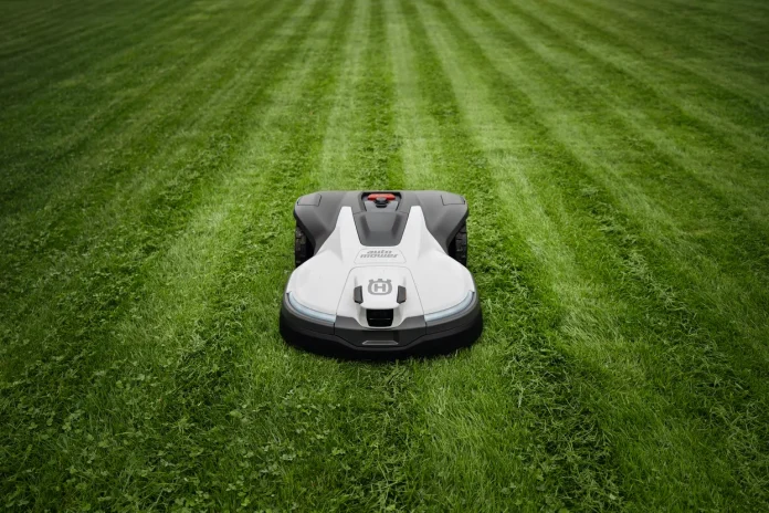 Ein weißer Husqvarna-Mähroboter fährt über einen sauber gemähten grünen Rasen mit deutlichen Spuren.