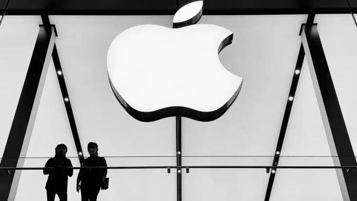 Großes, beleuchtetes Apple-Logo in einem modernen Geschäft mit zwei Personen als Silhouetten.
