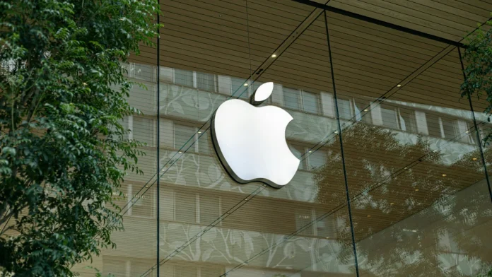 John Ternus Kurswechsel: Beleuchtetes Apple-Logo an einer Glasfassade mit Spiegelungen von Gebäuden und grünen Pflanzen.