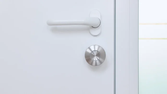 Silbernes Nuki Smart Lock an einer weißen Tür mit einem weißen Türgriff.