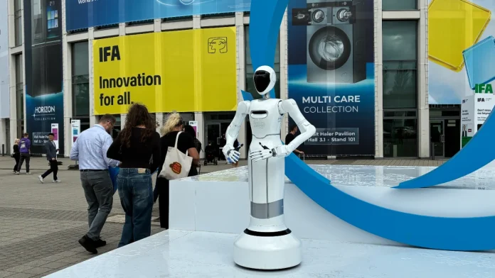 Weißer humanoider Roboter auf der IFA Berlin mit Innovationsbannern und Menschen im Hintergrund.