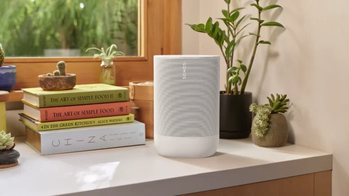 Ein weißer Sonos-Lautsprecher auf einer Kommode neben Kochbüchern und Zimmerpflanzen.