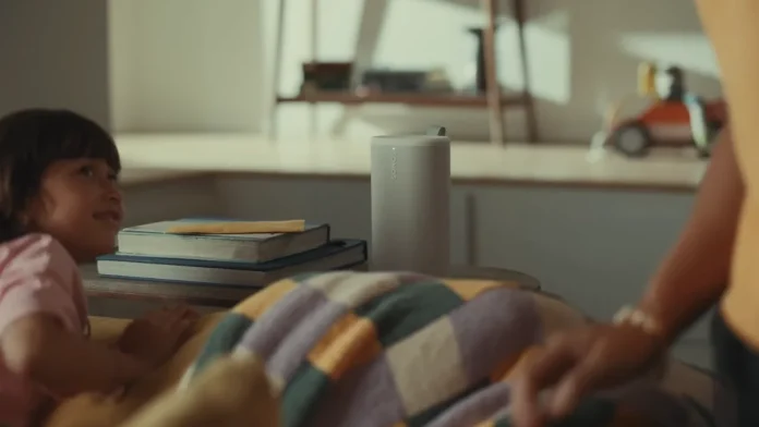 Ein weißer Sonos-Lautsprecher auf einem Tisch in einem gemütlichen Wohnzimmer mit einem Kind und Büchern.