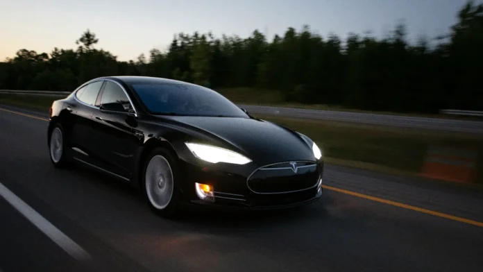 Schwarzer Tesla Model S fährt in der Dämmerung mit eingeschaltetem Licht auf der Autobahn.