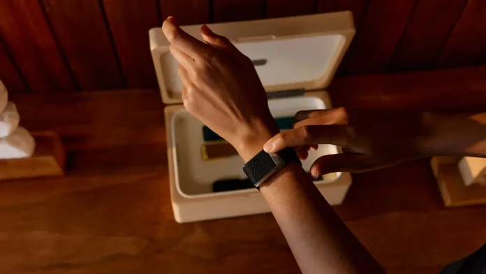 Person trägt einen schwarzen Whoop Fitnesstracker am Handgelenk neben einer Aufbewahrungsbox aus Holz.
