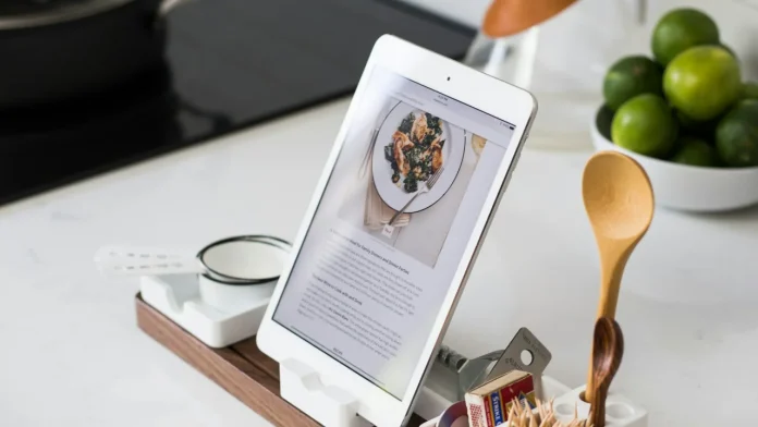 Ein iPad auf einem Holzständer auf einer Küchenarbeitsplatte neben einem Holzlöffel und Limetten