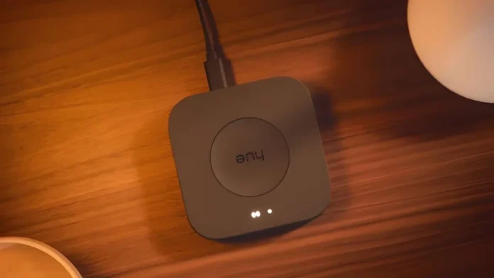 Philips Hue Bridge mit leuchtender LED auf einem Holztisch neben einer Lampe