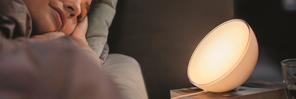 Smarte Tischleuchte auf Nachttisch neben schlafender Person im Bett